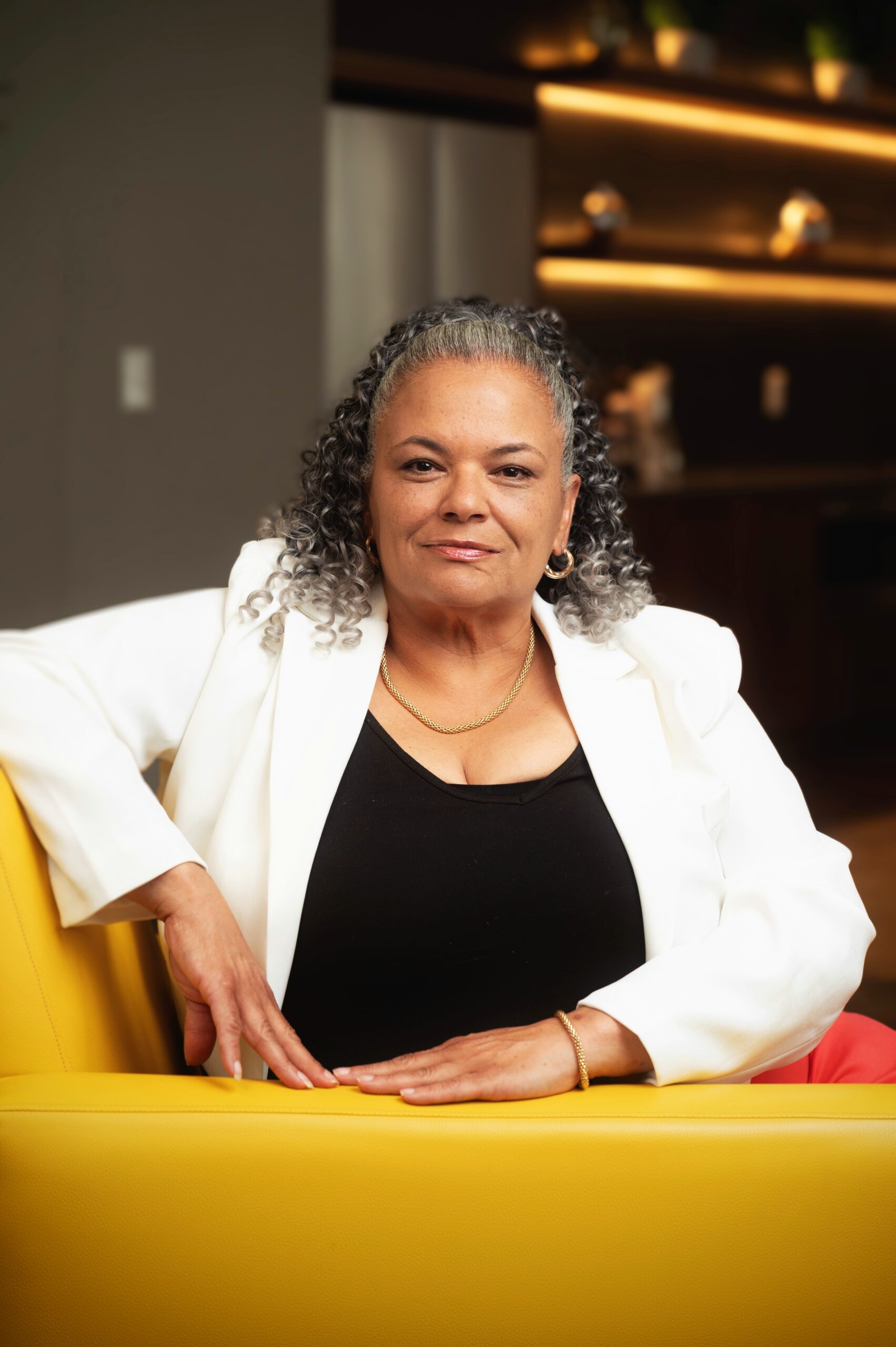 Confident woman in a white blazer sitting comfortably indoors.