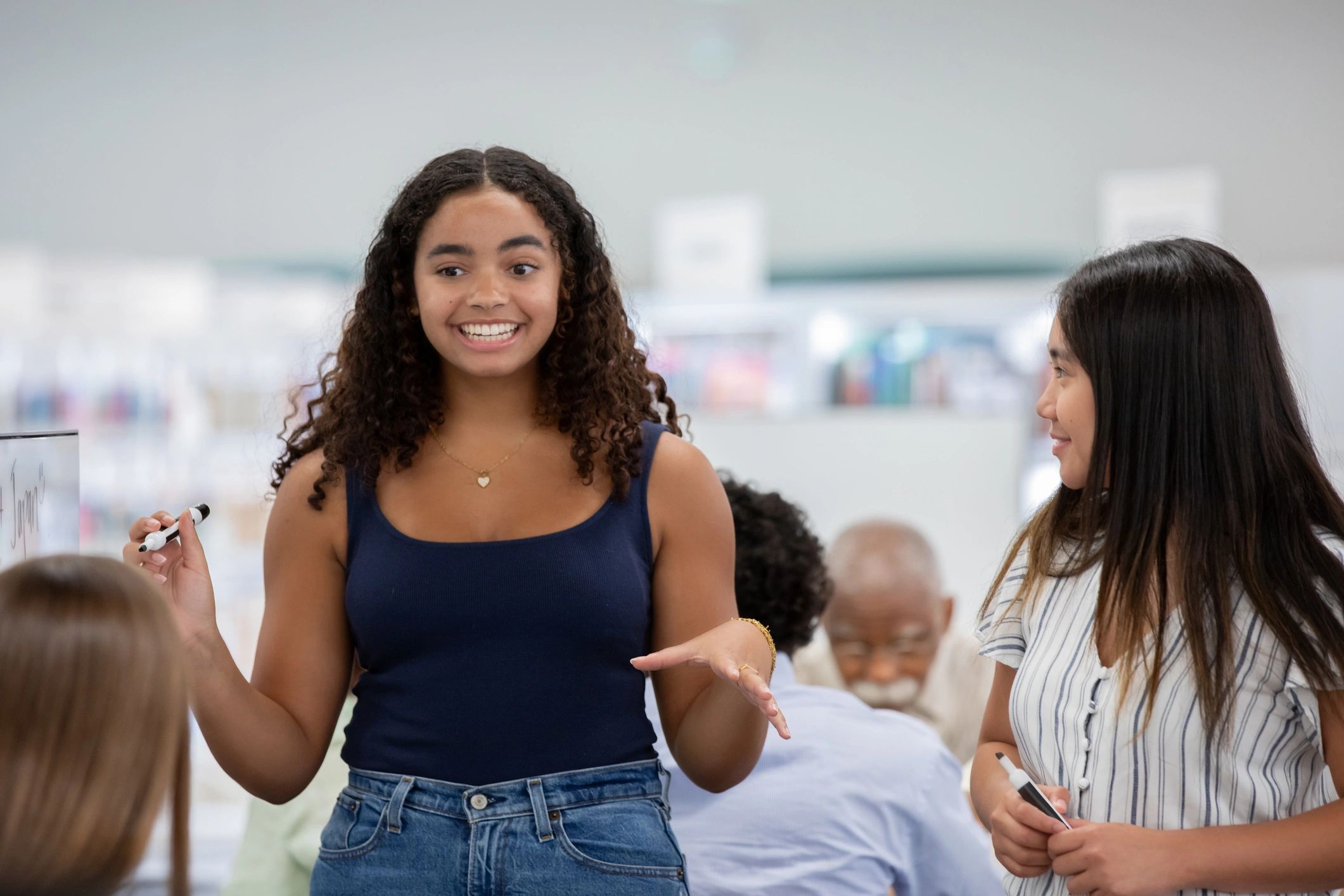 Young woman smiling and gesturing while talking to others indoors.