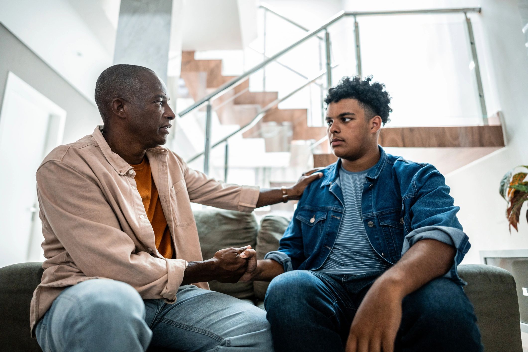Two men engaged in a serious conversation on a couch.
