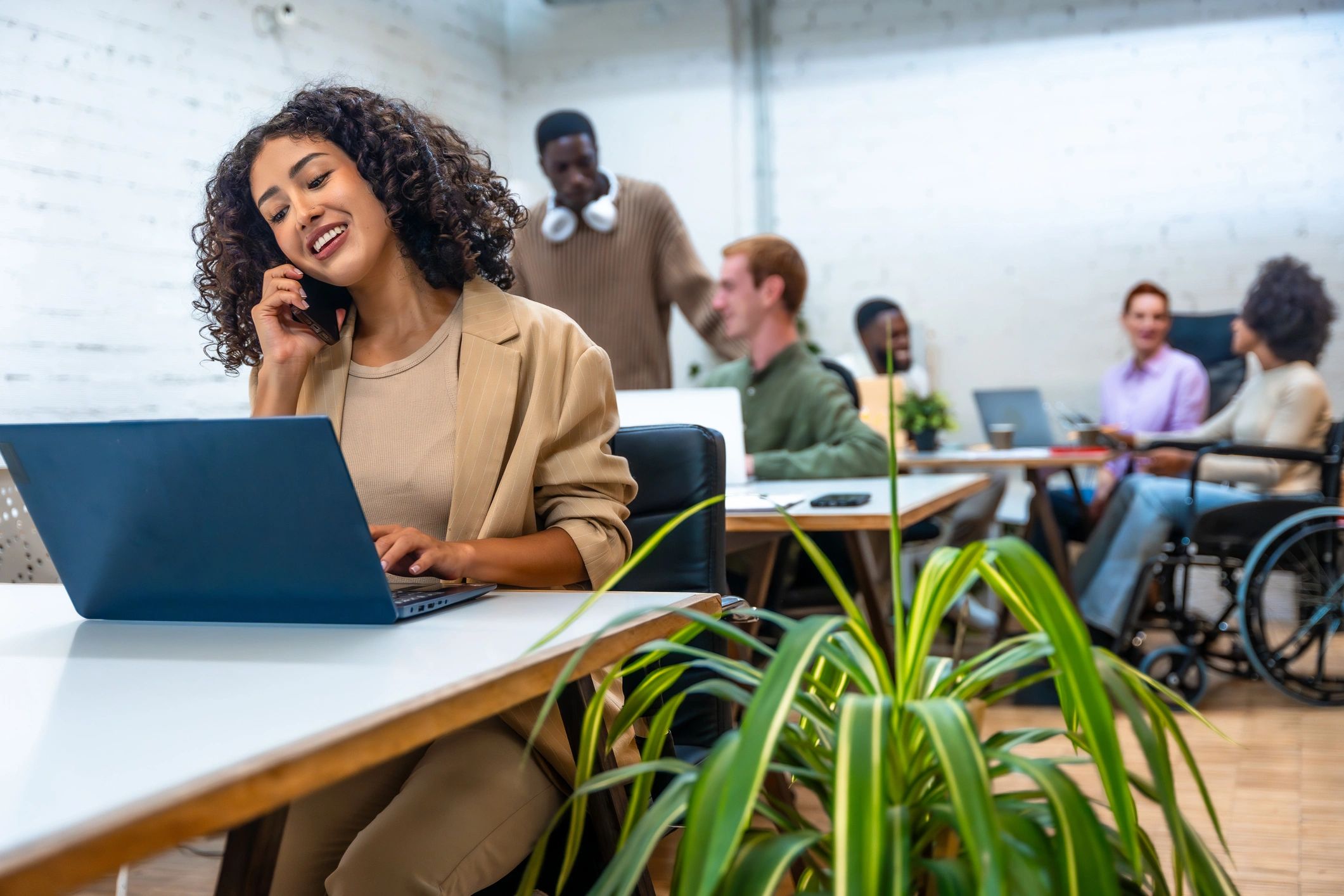 Woman talking on phone in a lively office with coworkers.