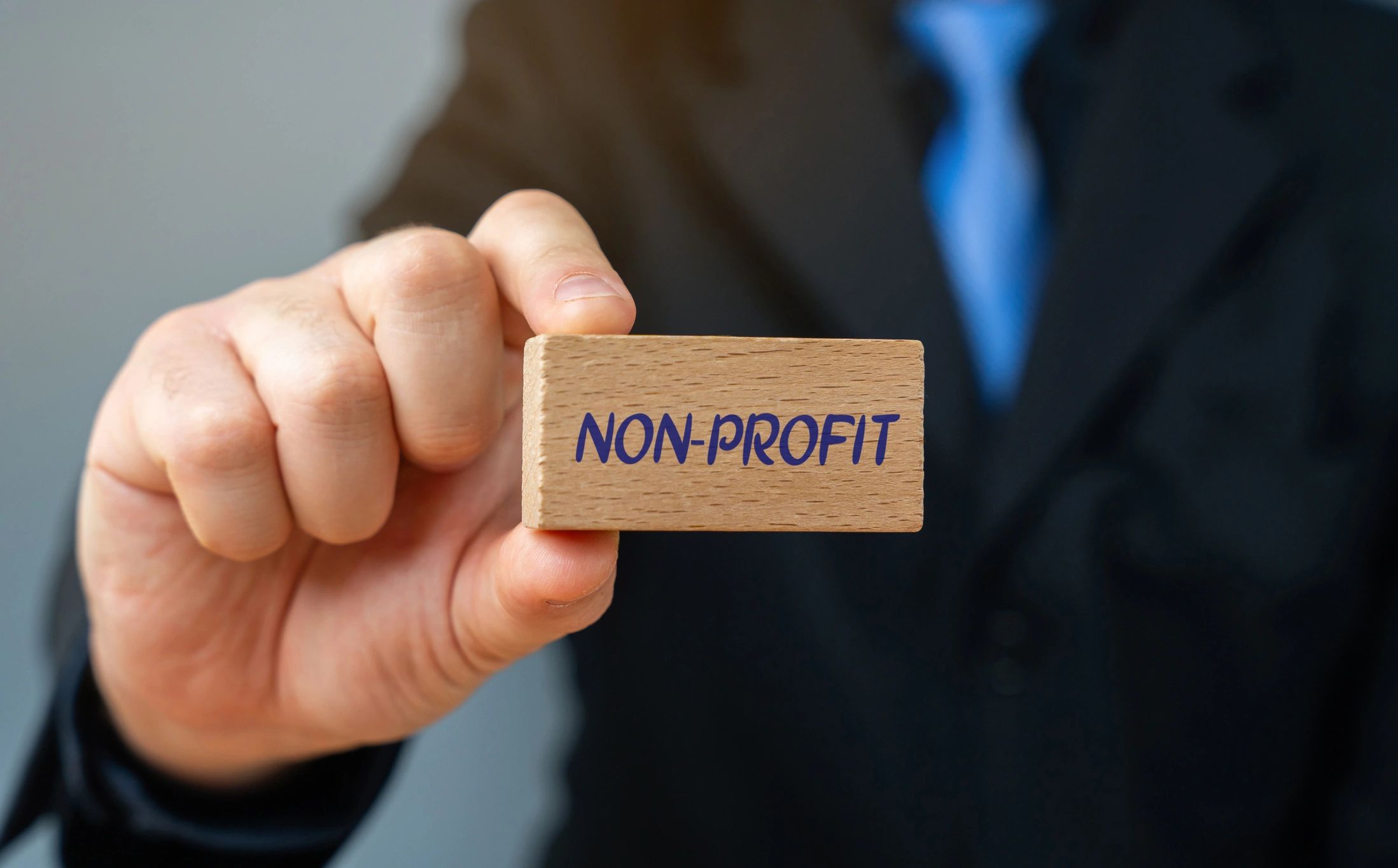 Hand holding a wooden block labeled 'NON-PROFIT' in business attire.
