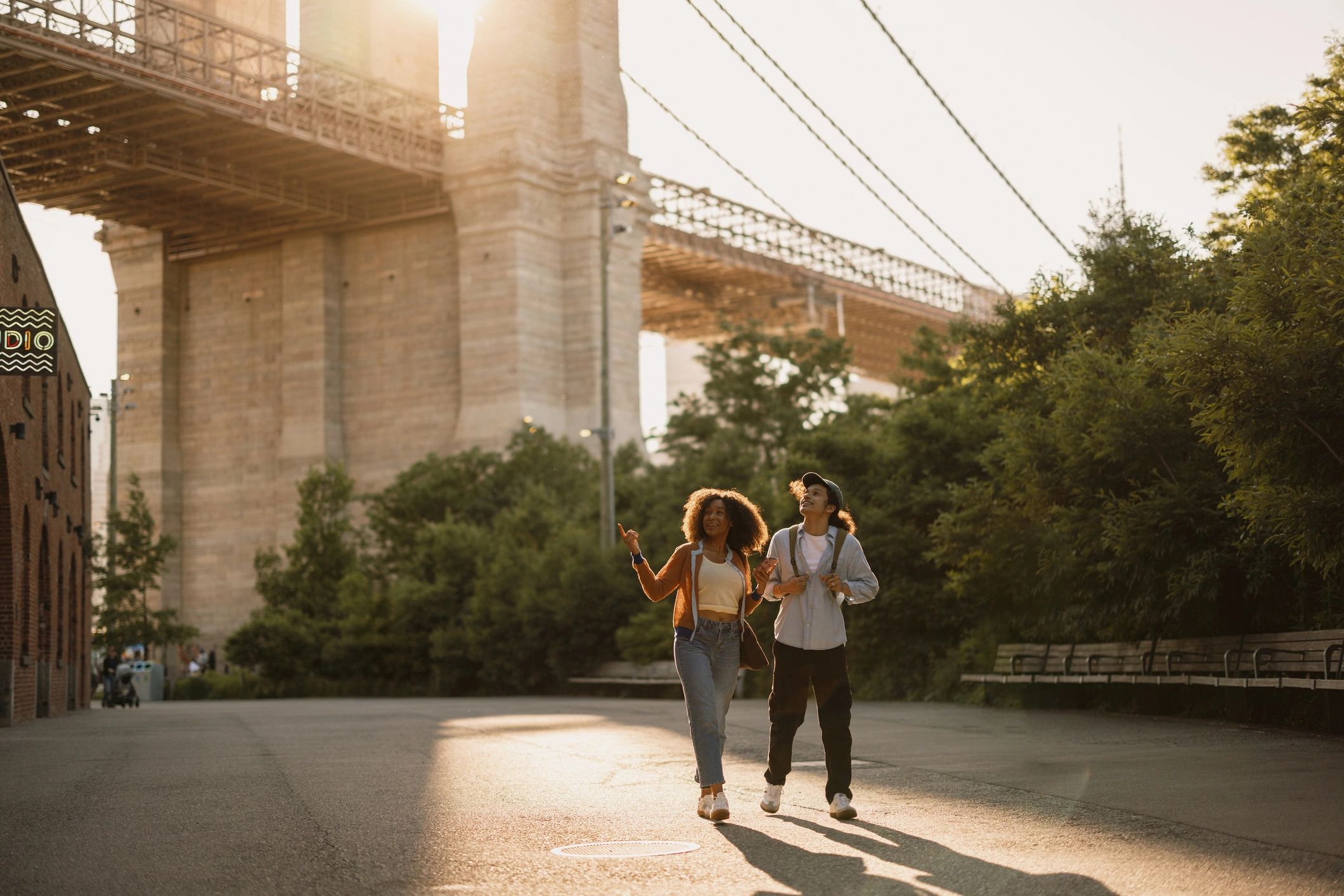 Couple walking hand-in-hand near a bridge at sunset.