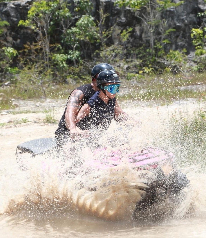 Person riding an ATV through muddy water splashes.