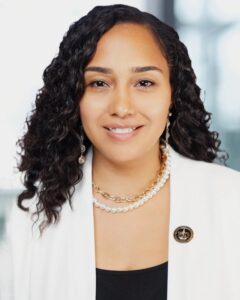 Confident woman with curly hair and a white blazer smiling.